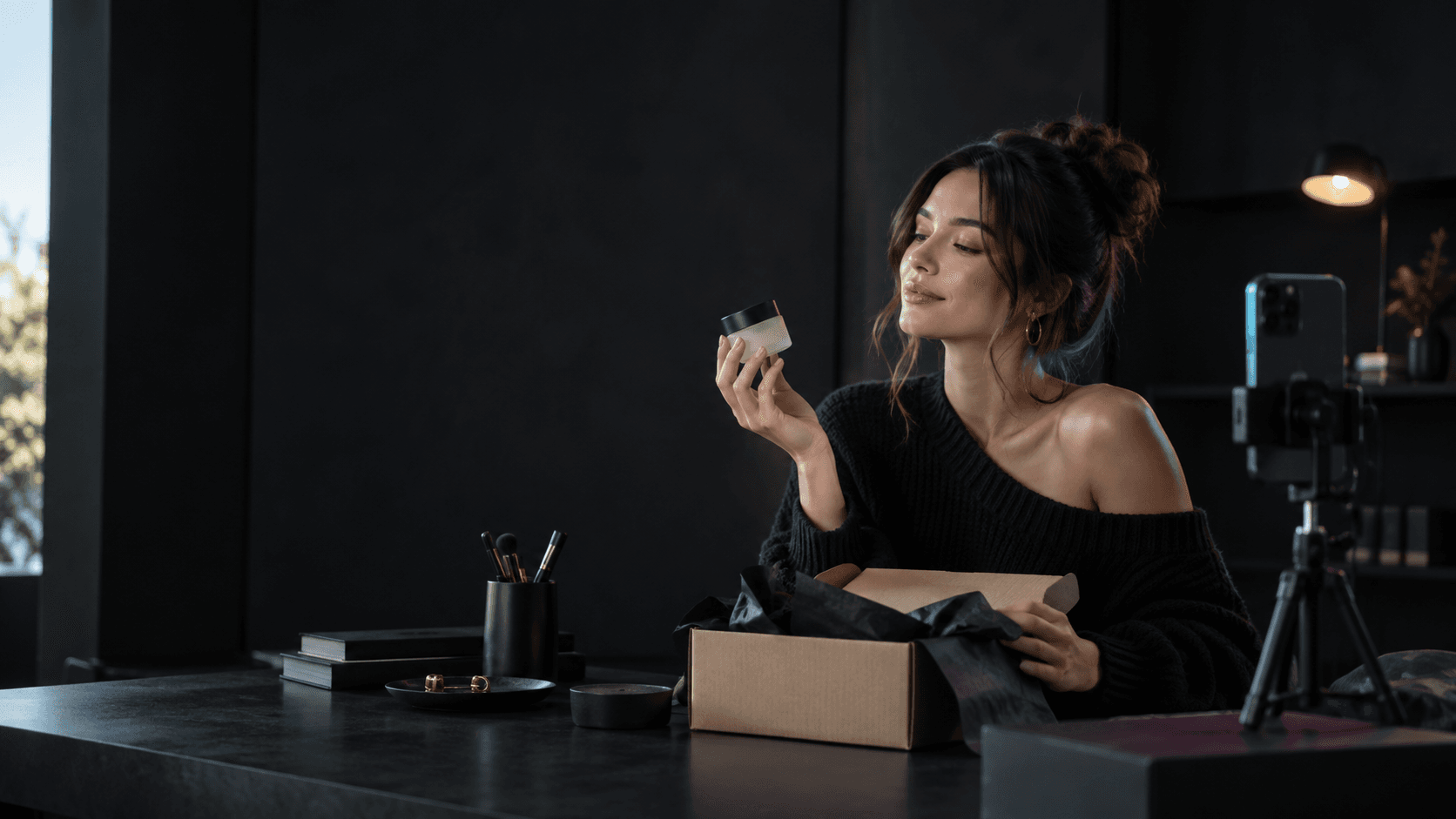 Créatrice découvrant un produit reçu en échantillon, téléphone sur trépied prêt à filmer